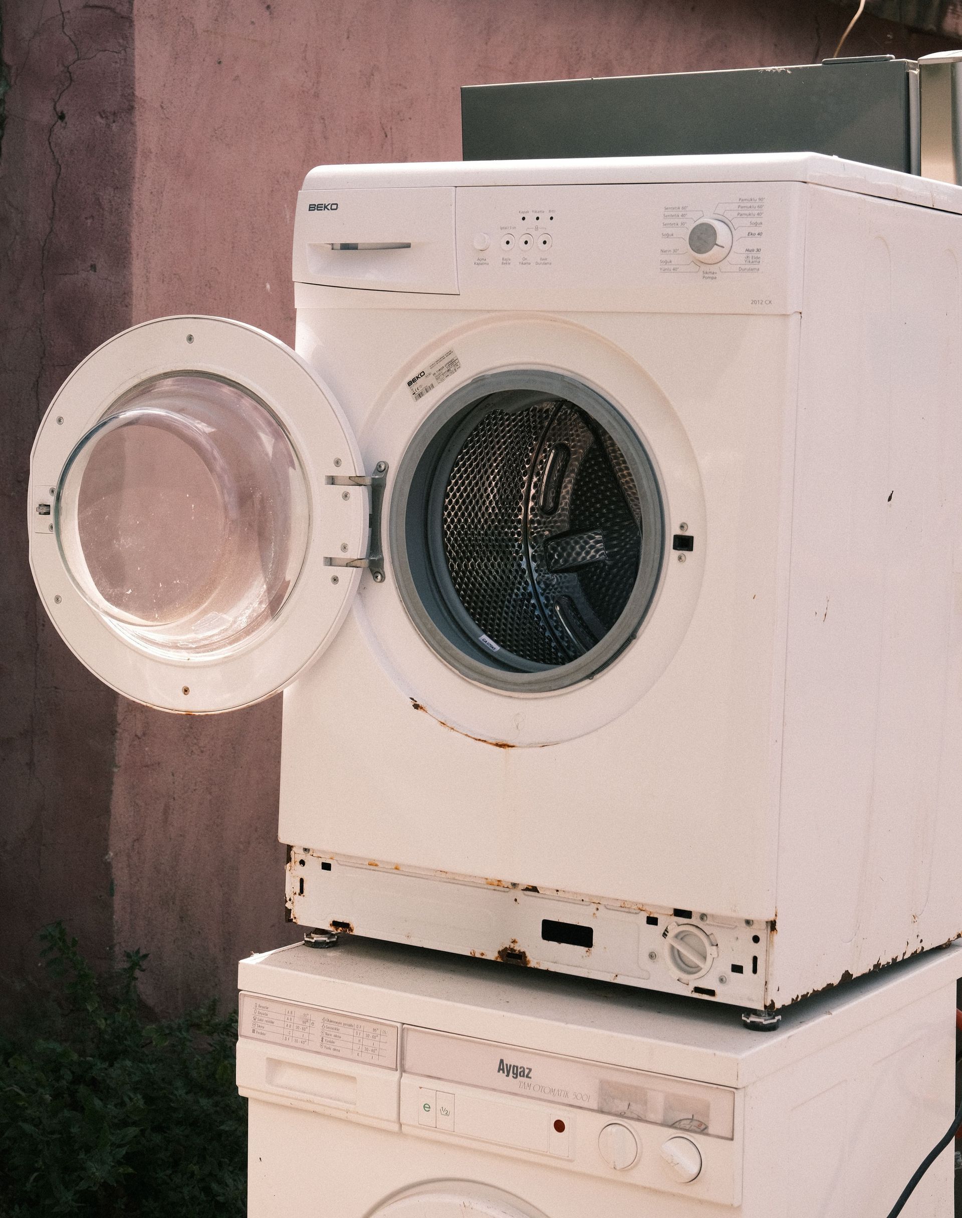Outdoor view of two stacked laundry machines with an open door, showing rustic surroundings.